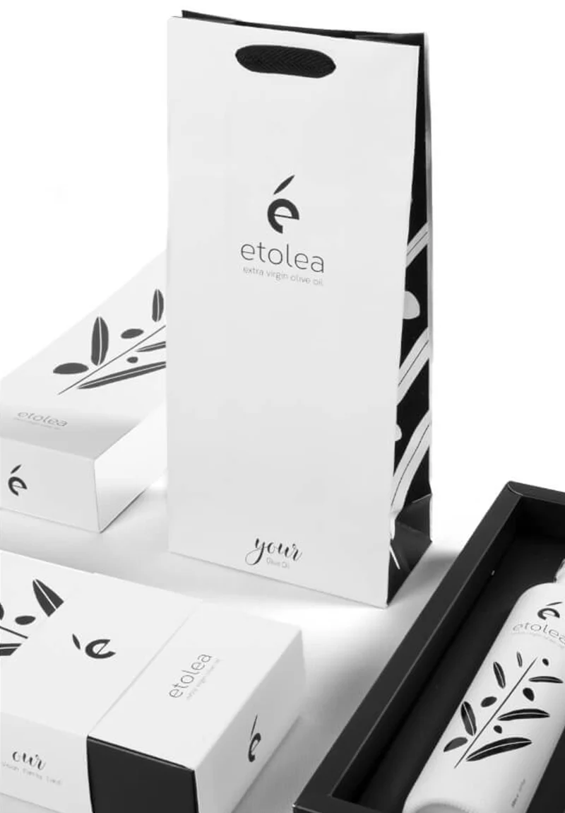 Bottle of Etolea Blend Black Extra Virgin Olive Oil with elegant packaging next to a decorative gift box and carry bag.
